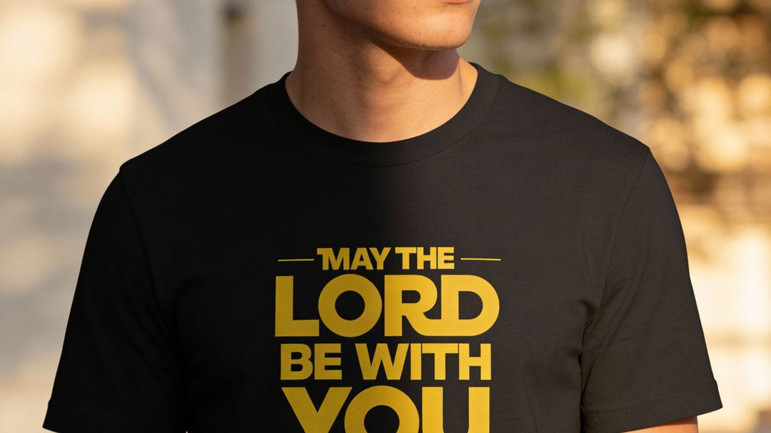 A person wears a black t-shirt with yellow text that says "MAY THE LORD BE WITH YOU."